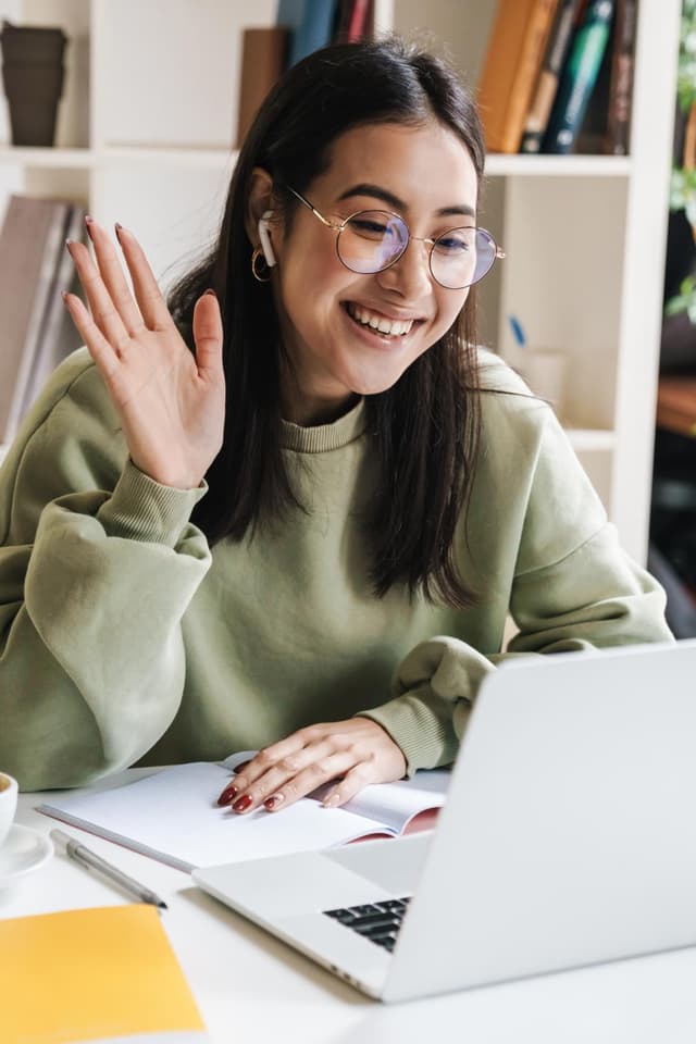 girl waving to laptop webcam during a video call